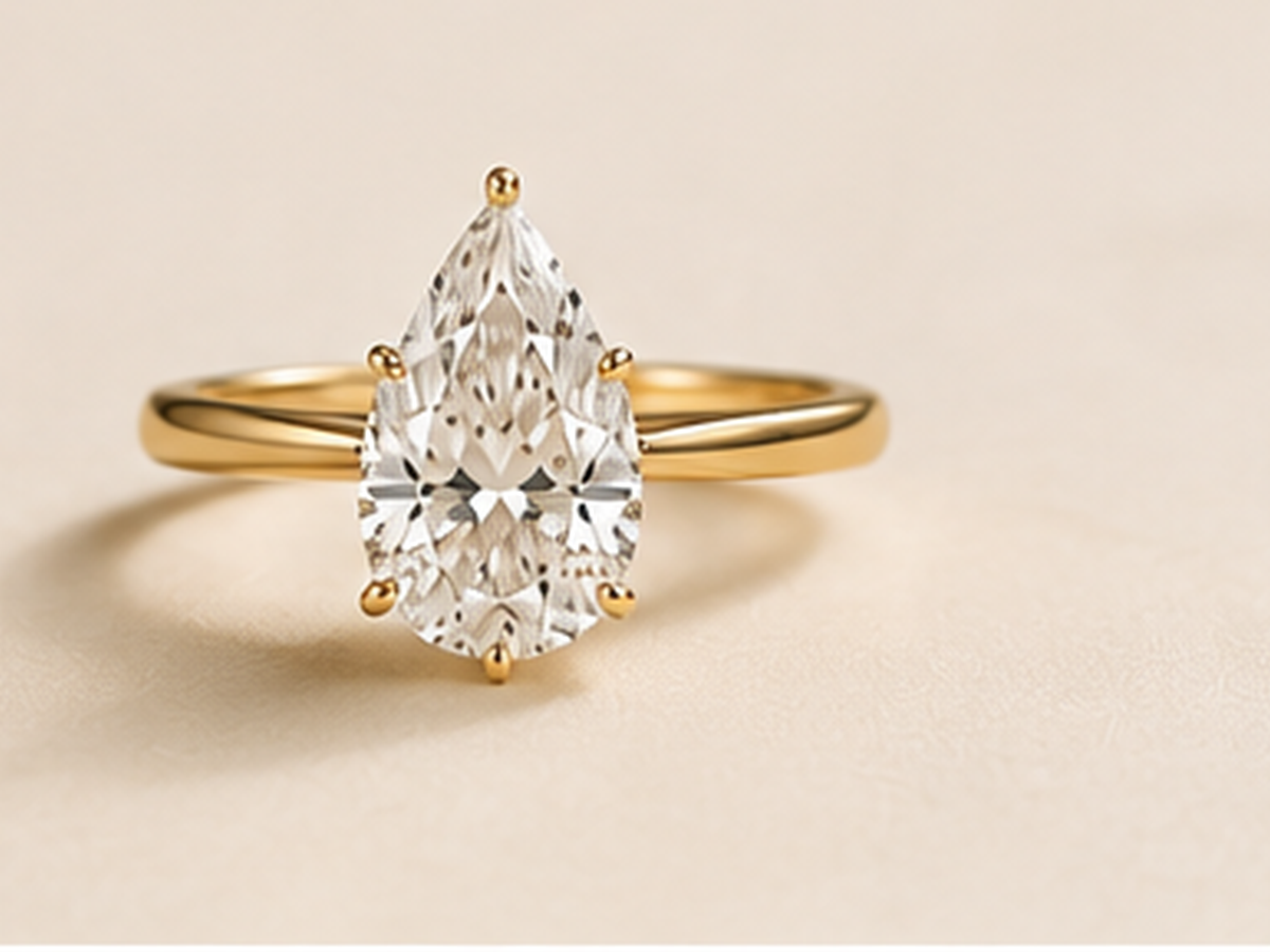 Pear lab-grown diamond engagement ring on a warm ivory background.